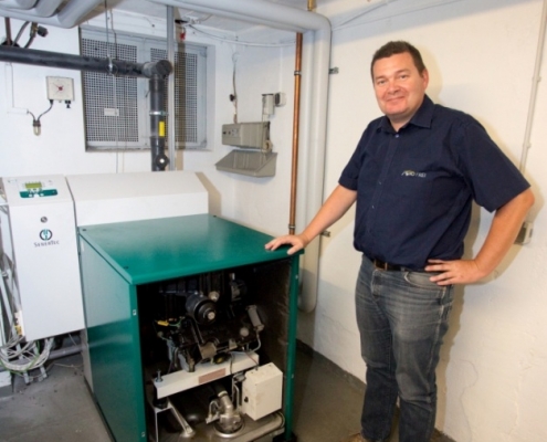 Geschaeftsfuehrer Herbert Frei steht neben seinem Dachs Blockheizkraftwerk, welches sein Autohaus mit Strom und Wärme versorgt.